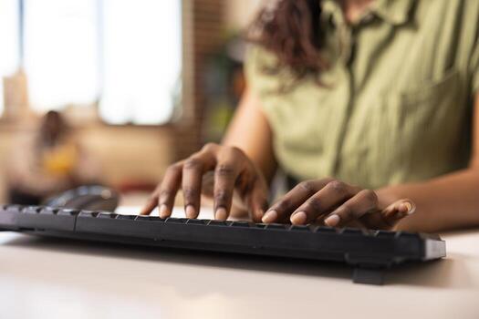 Close up of black female individual typing data on keyboard while working remotely. African american fingers pressing keys, entering details on computer and updating business reports. photo