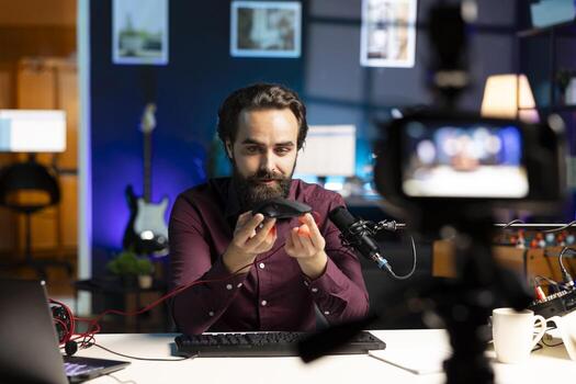 Tech guru filming technology review for internet channel in apartment studio, analyzing wired gaming mouse for audience. Viral online star looking at computer peripheral device during vlog photo