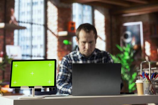 Teleworker in home office completing spreadsheets on laptop next to mockup tablet, entering data, calculating totals. Close up of green screen device next to bookkeeper using spreadsheet software photo