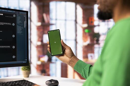 Man holding mockup phone solving personal tasks with AI LLM chatbot answering prompts. Person using green screen smartphone and computer to interact with large language model program photo