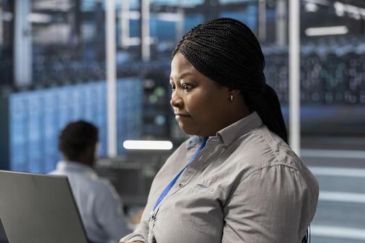 Engineer using notebook device to oversee data center machines processing workloads. African american woman doing maintenance on server rigs tasked with solving complex operations photo