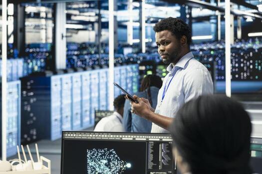 Data center technician looks at AI visualization dashboard to pinpoint equipment performance issues. African american man in server hub looks at data analysis graph to reduce hardware failures photo
