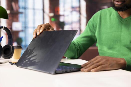 Remote employee in home office using laptop, preparing presentation slides, adjusting layouts. Close up of african american teleworker finishing company project, saving files on notebook photo