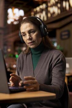 mujer estudiante saludo su profesor en un ordenador portátil web llamar, asistiendo un Universidad clase desde el biblioteca. erudito tomando notas para un colegio asignación como parte de remoto mi aprendizaje programa. foto