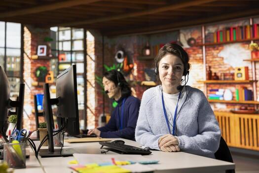 Portrait of smiling call center employee wearing headset resolving customers concerns, speaking into microphone. Happy customer service worker using headphones mic processing clients orders photo