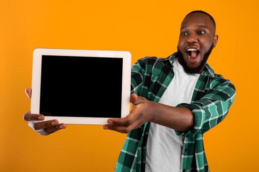 Excited African Guy Showing Digital Tablet With Big Blank Screen To Camera Recommending Great Application Posing In Studio Over Yellow Background. Gadget Advertisement With Computer Display. Mockup photo