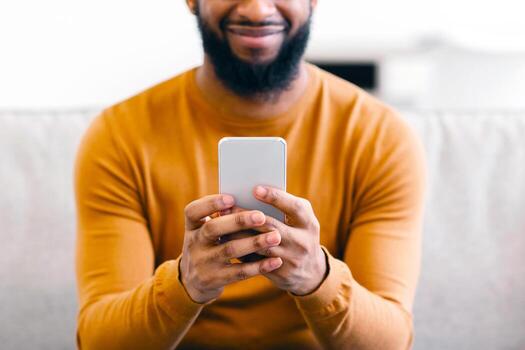Unrecognizable Black Guy Using Mobile Phone Testing New Application Browsing Internet And Texting Sitting On Sofa At Home. Smartphone Gadget And Modern Communication. Cropped, Focus On Cellphone photo
