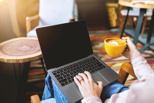 Unrecognizable lady typing on laptop computer with blank screen, mockup image with copy space, sitting in cafe, surfing internet and drinking coffee, crop photo