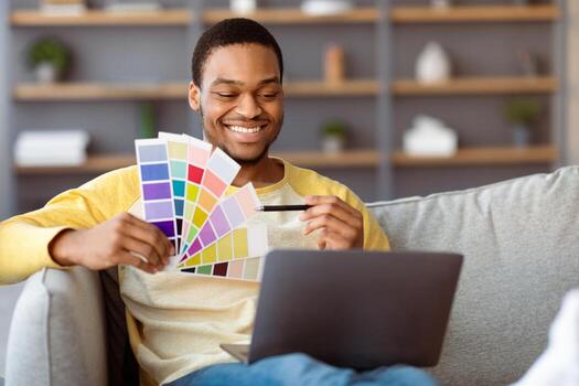 contento exitoso negro chico web diseñador teniendo llamada desde hogar, utilizando ordenador portátil mientras sentado en sofá en vivo habitación, hablando a negocio socios, demostración color paleta y sonriente, Copiar espacio foto