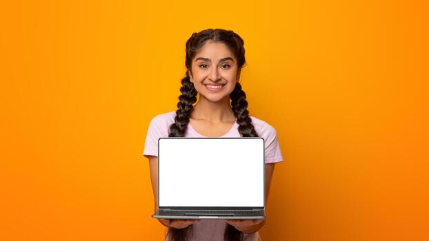 Great Website. Smiling Indian Lady Holding And Showing Laptop Computer With Empty Screen To Camera, Posing Standing Over Yellow Studio Background. Digital Display, Mockup For Advert photo