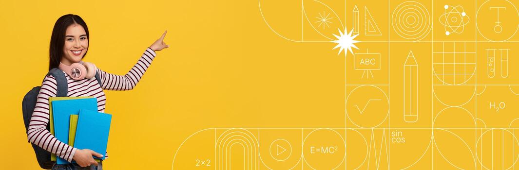 Asian student stands smiling and pointing, holding books and a folder in a lively classroom. The bright yellow background enhances the atmosphere of learning and curiosity. photo