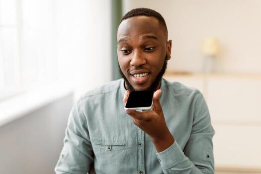 Black Business Guy Using Cellphone With Voice Assistant App Or Chatting Via Loudspeaker Mode Sitting At Workplace In Office. IOT, Modern Communication Application Concept photo