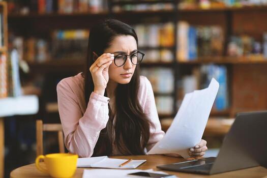 Pensive woman entrepreneur working with papers and laptop computer at cafe, having problem and checking documents while sitting at table. Financial manager having difficulties with job photo