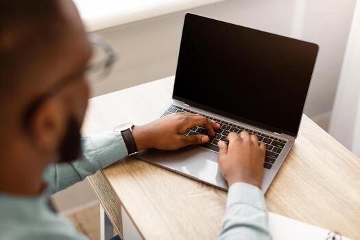 High-Angle Back View Of Black Businessman Using Laptop With Empty Screen Typing On Keyboard Sitting At Workplace In Modern Office. Business Website Ad. Selective Focus On Computer, Mockup photo