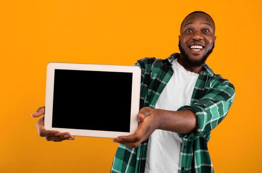 Joyful African Man Showing Empty Digital Tablet Screen To Camera Recommending New Application Standing Over Yellow Studio Background. Advertisement Banner With Tablet Computer Display Mockup photo