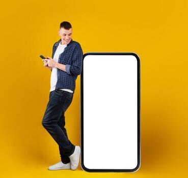 Man Near Big Cellphone Standing Using New Application On His Mobile Phone Browsing Internet And Texting Looking At Huge Empty Screen On Smartphone On Yellow Background In Studio. Square photo