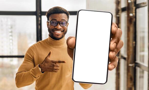 Mobile app advertisement. Black man showing and pointing at big white empty smartphone screen, standing in office, mockup, closeup. Check this out, cellphone display template photo