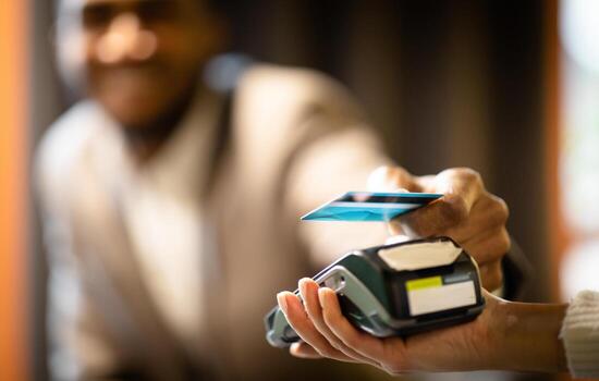 NFC Technology. Smiling afro manager in suit giving credit card to waitress using modern contactless system at the bar photo