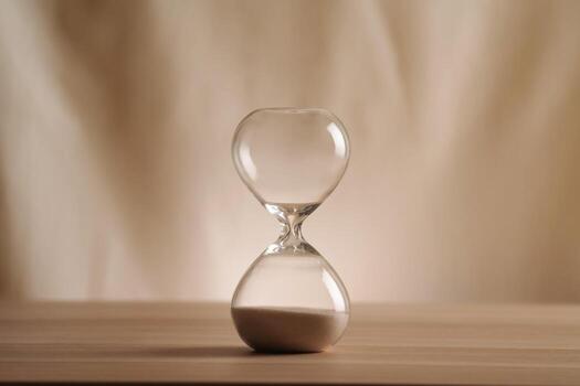 A simple hourglass on a wooden table with a beige backdrop, symbolizing time flow and minimalistic living. Represents timeless themes in a creative, uncluttered presentation for stylish concepts. b photo