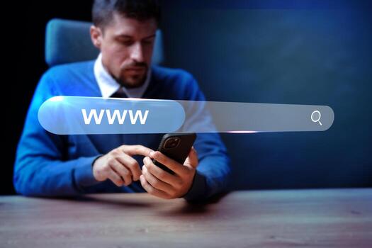 Man using smartphone at desk with search bar and digital interface in a modern office setting during evening hours photo