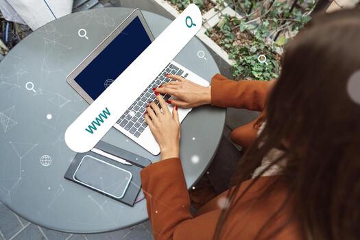 Woman using laptop at outdoor table surrounded by greenery to search online in a modern urban setting photo