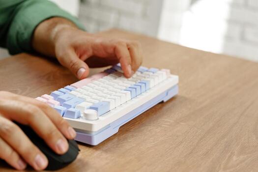 Hands typing on a pastel keyboard while using a computer mouse on a wooden desk photo