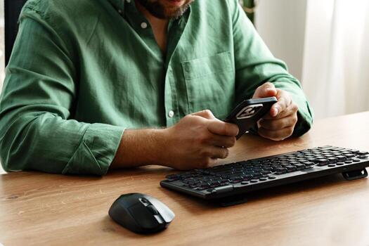 Man using smartphone while seated at wooden desk with keyboard and mouse in modern workspace photo