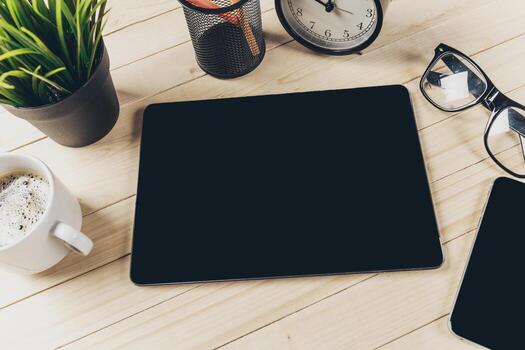 Workspace setup with tablet, coffee cup, clock, and glasses on wooden table photo