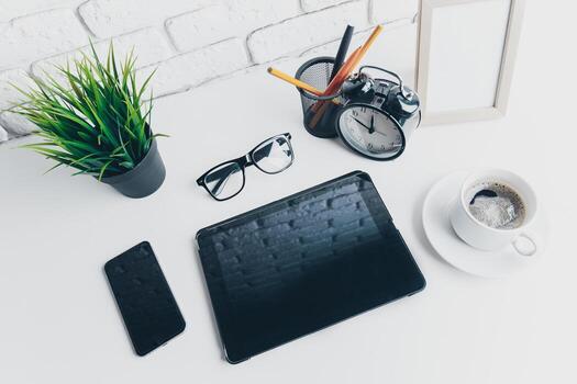 Workspace setup featuring tablet, smartphone, and coffee on a desk with greenery and clock photo