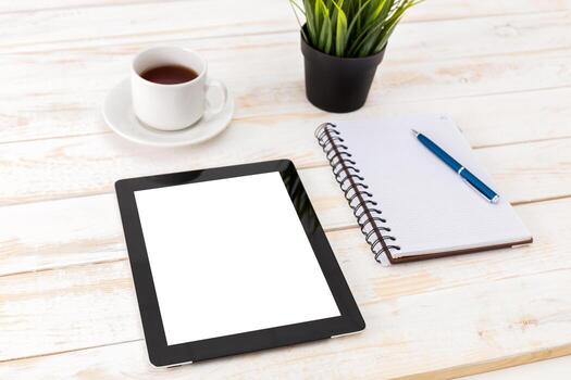 Coffee and workspace setup on a wooden table with a tablet and notebook photo