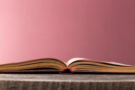 Open book resting on a table with a blurred pink background highlights reading activity photo