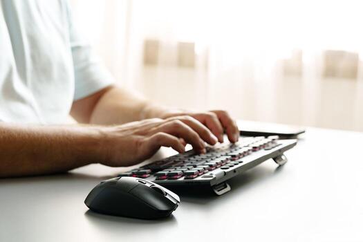 Hands typing on a keyboard with a computer mouse resting beside it in a bright room photo