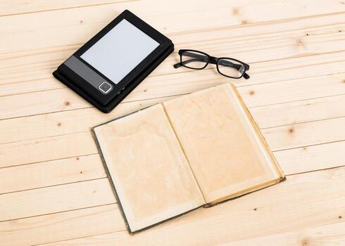 Digital and traditional reading setup with e-reader, empty book, and glasses on wooden table photo