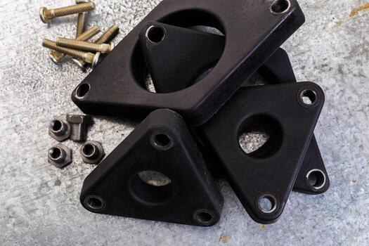 Black triangular rubber components with bolts on a gray surface in a workshop setting photo