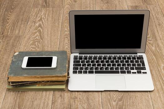 Digital workspace with laptop and smartphone on stack of old books in a cozy setting photo