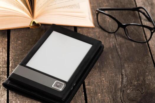 Reading session with an e-reader, glasses, and an open book on wooden table photo