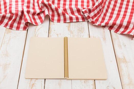 Blank notebook rests on red and white checkered tablecloth in bright, rustic setting photo