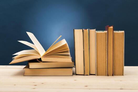 Open book resting on a stack with several closed books on a wooden table photo