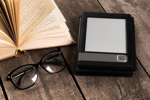 Reading setup with e-reader, glasses, and open book on wooden table photo