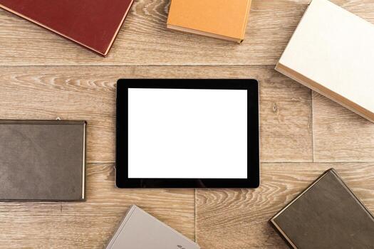 Digital device surrounded by various books on a wooden surface in a cozy setting photo
