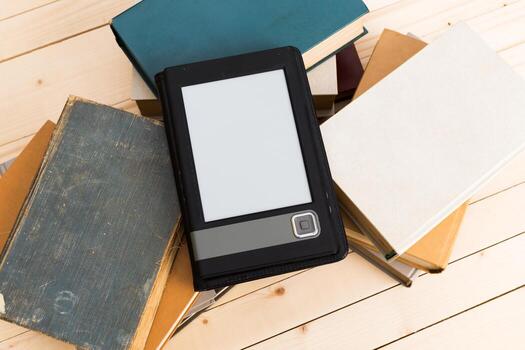 Digital reader placed on top of a stack of books on a wooden table photo