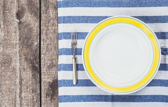 Setting a dining table with a striped mat, empty plate, and silver fork ready for a meal photo