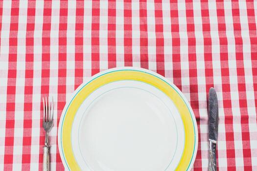 Table setting with empty plate and silverware on a red checkered tablecloth photo