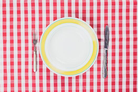 Table setting with empty plate on checkered red and white tablecloth in bright light photo