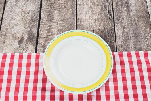 Empty plate on a red checkered tablecloth in a rustic setting during daytime photo