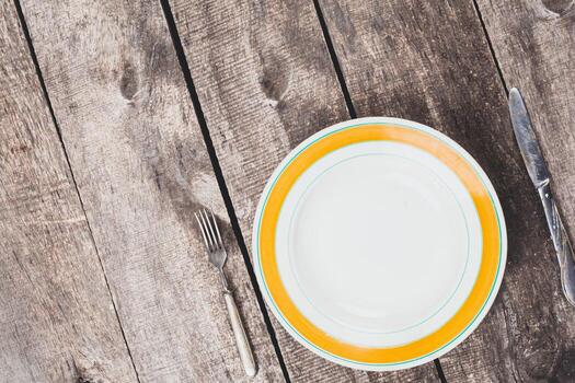 Table setting with an empty plate, fork, and knife on rustic wooden surface photo