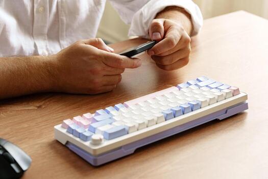 Person using smartphone while sitting at desk with a colorful keyboard in a bright room photo