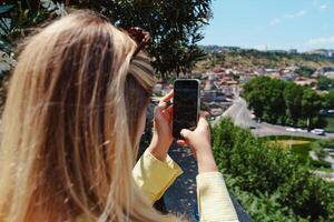 mujer toma foto de ciudad ver desde cima de la colina en un soleado día en verano, exhibiendo un vibrante paisaje y urbano vida