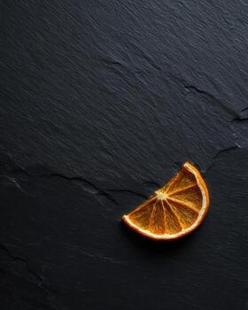 Dried orange slice resting on dark textured surface photo