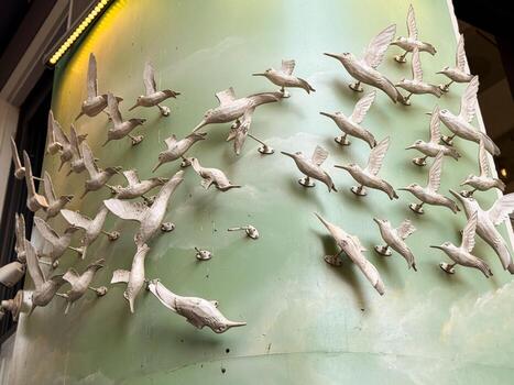 White bird sculptures attached to a green wall creating an impression of flock in flight. Symbolism of freedom, motion, and collective unity represented in design. photo